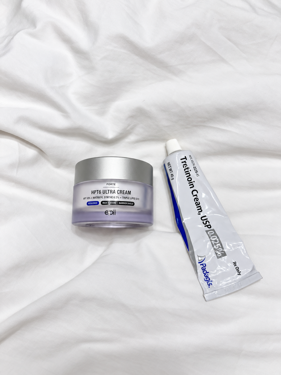 Tretinoin 0.025 percent cream and Epii HPT6 Ultra Cream on white fabric